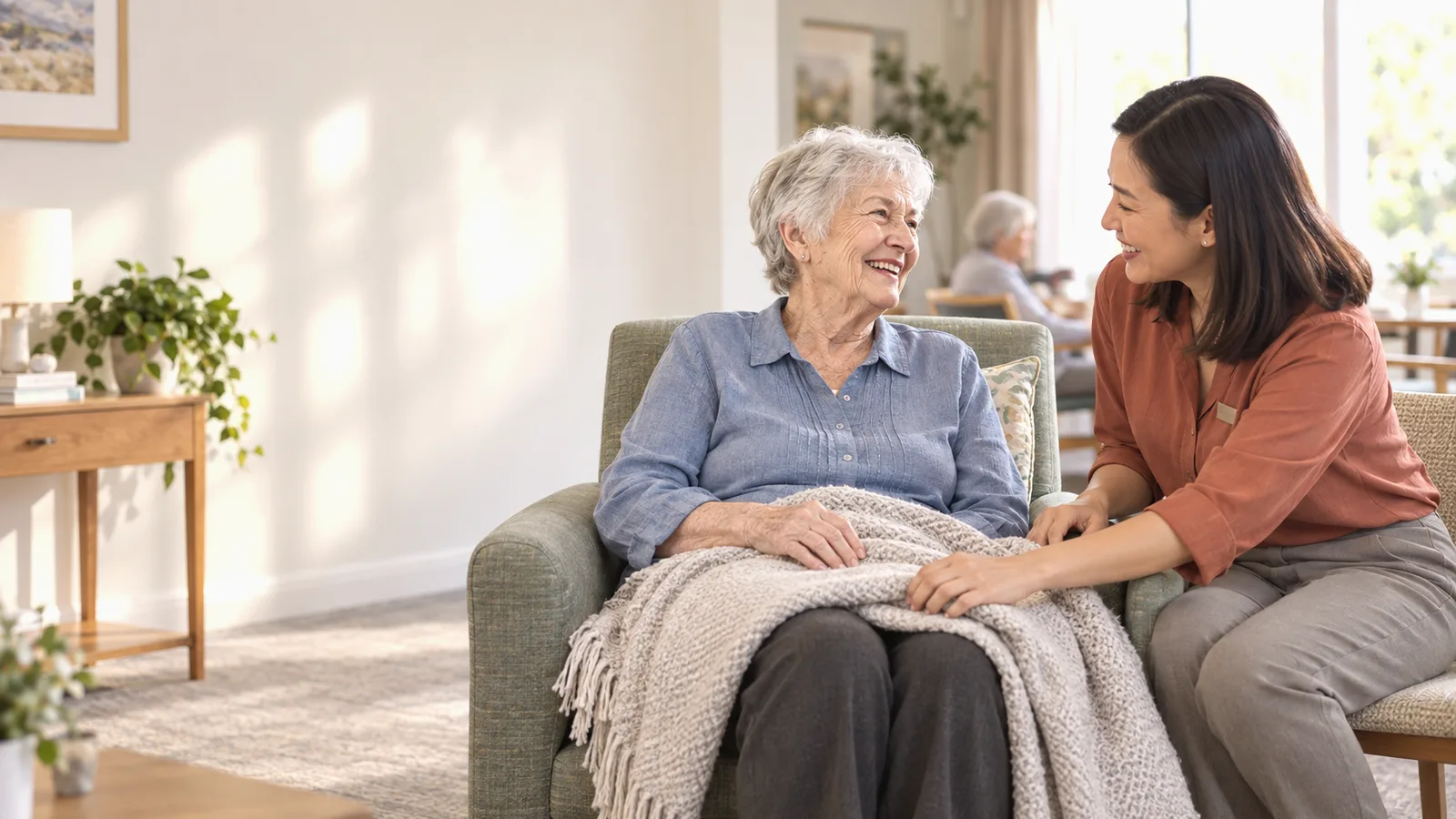 An aged care staff member checking on a resident settled with a blanket in a lounge
