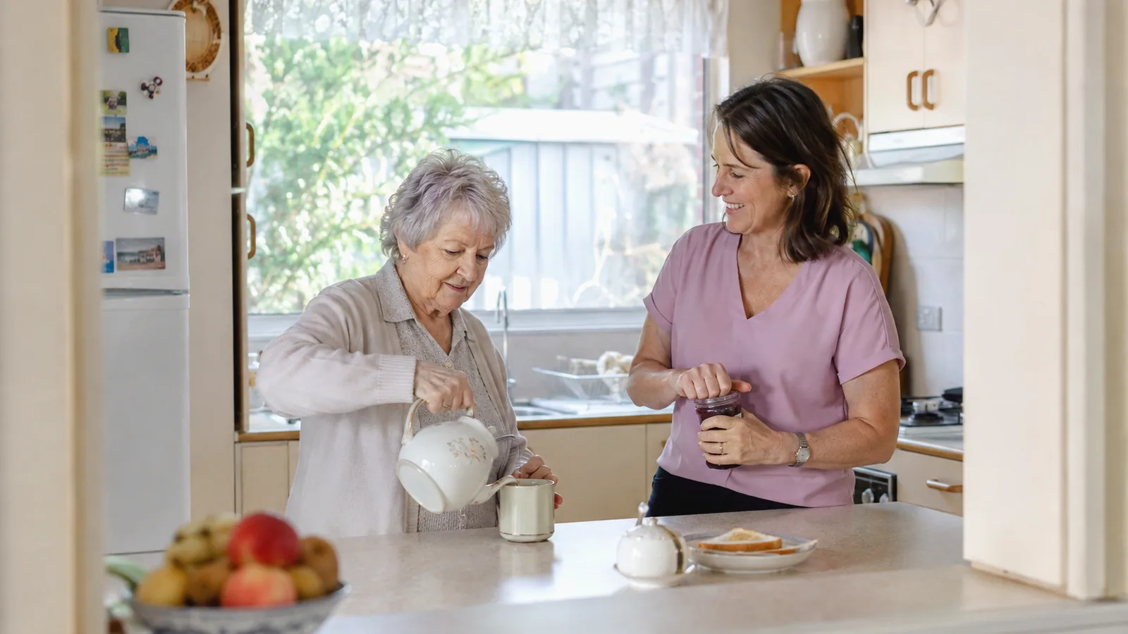 A home care support worker helping an older woman in her kitchen at home